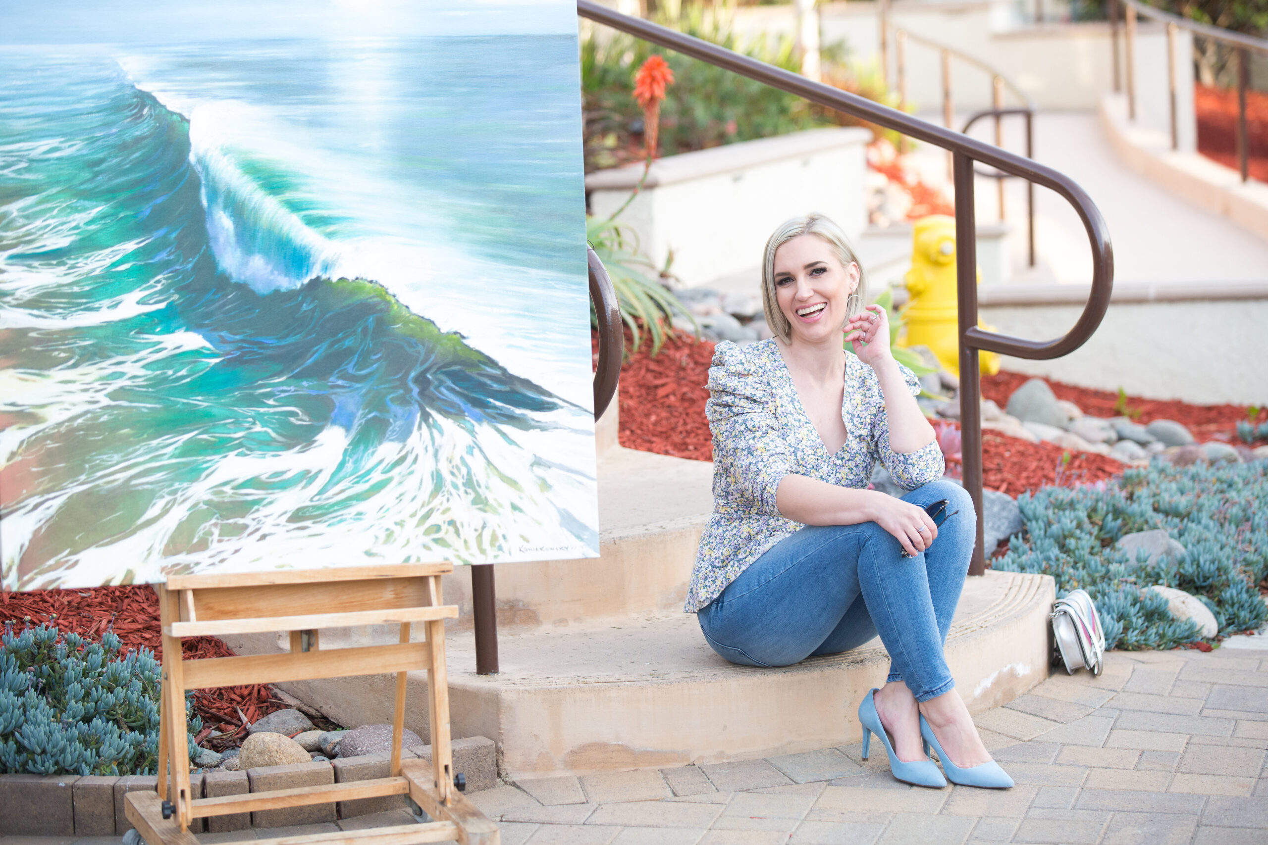 Jaquelyn Wahidi wears a statement top in next to a painting of the Ocean in Solana Beach, California.