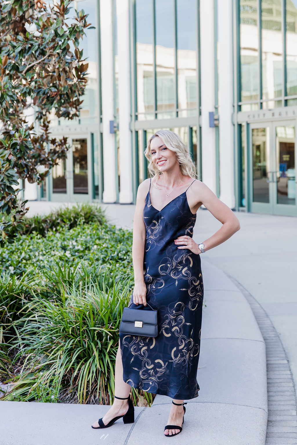 Personal stylist Jaquelyn Wahidi wears a black and gold slip dress in front of a San Diego civic building.