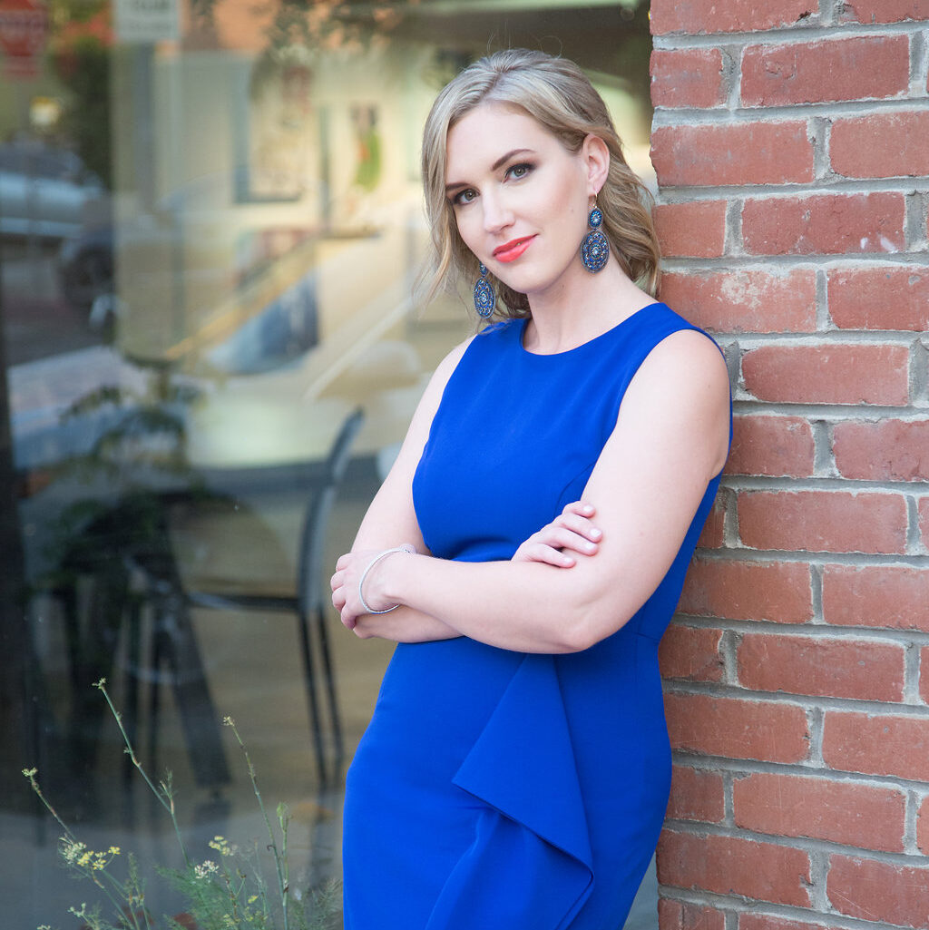 Del Mar Personal Stylist Jaquelyn Wahidi poses in a blue dress against a brick wall