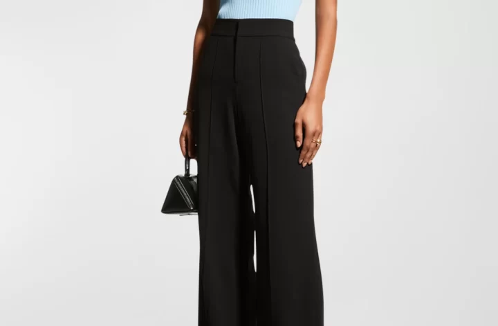 A model wears sleek black wide leg pants with a blue sweater tank and black handbag.